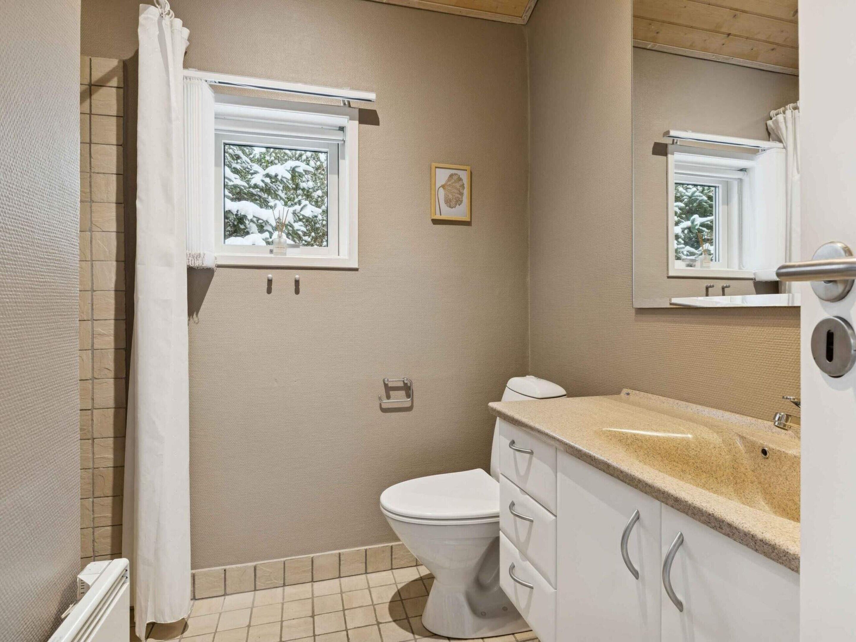 A bathroom with a toilet, a sink, a window, and a shower curtain.