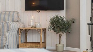 Ein Zimmer mit einer gestreiften Couch, einem an der Wand montierten Fernseher, einem kleinen Tisch mit Kerzen und einer Zimmerpflanze.