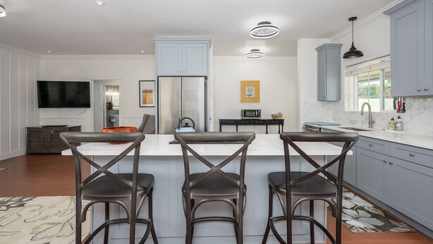 A modern kitchen with a central island, bar stools, a flat-screen TV, and a refrigerator. - Wonderful 2-bedroom house with Zonal Mini Splits , tree lined nieghborhood (Phoenix)