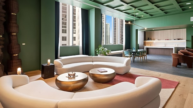 Ein modernes Wohnzimmer mit einem gebogenen weißen Sofa, zwei runden Couchtischen, einem kleinen Beistelltisch mit einer Kerze und Blick auf eine Stadtlandschaft durch große Fenster.