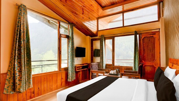 A wooden-paneled bedroom with a large bed, two windows, a flat-screen TV, and a wooden desk.