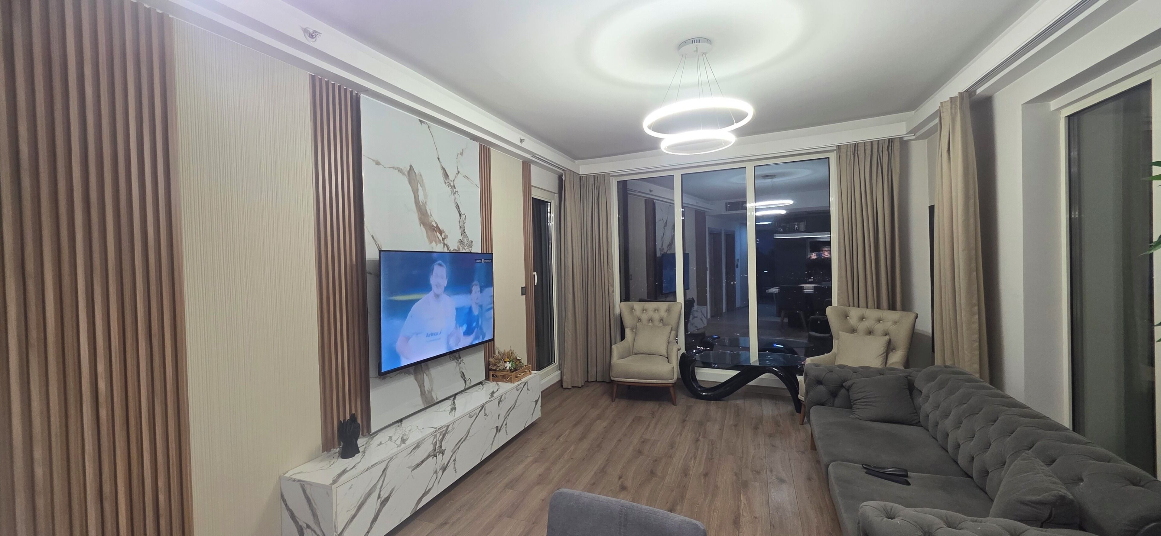 Un salon moderne avec un téléviseur à écran plat, un canapé, un fauteuil et une table basse en verre.