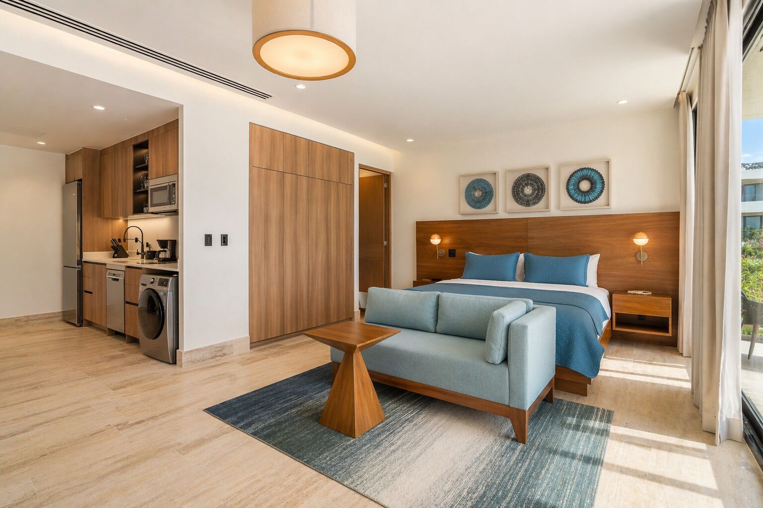 Une chambre d’hôtel moderne équipée d’un lit, d’un canapé, d’une petite table, d’un coin cuisine et d’une grande fenêtre.