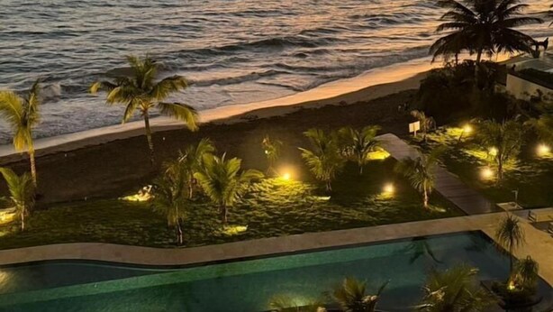 Un complexe hôtelier doté d’une piscine, de palmiers et offrant une vue imprenable sur l’océan au coucher du soleil.