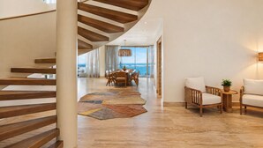 Un intérieur moderne avec un escalier en colimaçon, un coin repas et un espace salon offrant une vue sur l’océan.