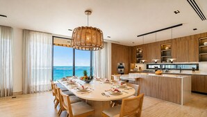 Une cuisine moderne avec des meubles en bois, un îlot central et un coin repas offrant une vue sur l’océan.