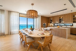 A modern kitchen with wooden cabinets, a central island, and a dining area with a view of the ocean. - Eden Cabarete  (Cabarete)