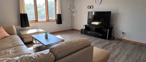 A living room with a sofa, a coffee table, a TV, and a window with curtains.