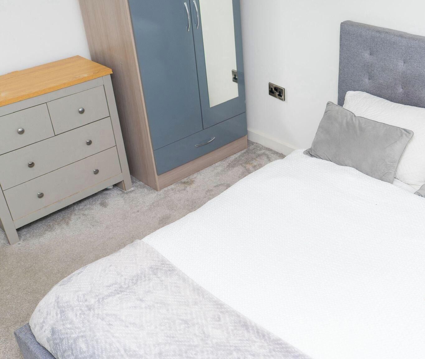 Een slaapkamer met een bed, een dressoir, een kledingkast en een nachtkastje.