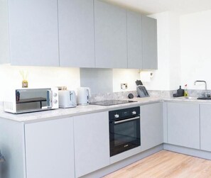 A modern kitchen with grey cabinets, a built-in oven, a microwave, and a toaster. - Bespoke Piccadilly 2-Bed Retreat Gym Spa Pool (Manchester)