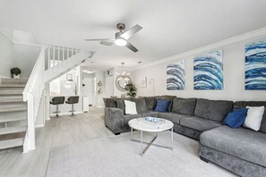 A modern living room with a grey sofa, a coffee table, and a staircase with white railings. - Cozy 2 bdr 2.5 bath beachfront complex condo (Cape Canaveral)