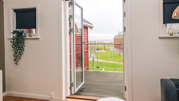 A room with a sliding glass door leading to a balcony with a view of a red building and grassy area. - 8 Person Holiday Home in Hadsund (Hadsund)