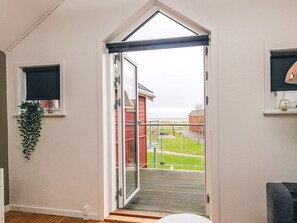 Una habitación con puerta de vidrio corredera que da a un balcón con vistas a un edificio rojo y una zona verde.