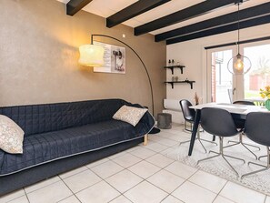 A modern living room with a dark sofa, a dining table with chairs, a hanging light fixture, and a wall-mounted shelf. - 8 Person Holiday Home in Hadsund (Hadsund)