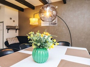 A dining table with a green vase of yellow flowers, a black chair, a lamp, and a wall-mounted shelf with candles. - 8 Person Holiday Home in Hadsund (Hadsund)