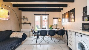 A modern kitchen with a built-in washing machine, a dining area with a table and chairs, and a black sofa with a floral pillow. - 8 Person Holiday Home in Hadsund (Hadsund)