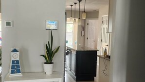 A modern kitchen with dark cabinetry, a central island, pendant lighting, and a white wall clock. - Rexford Sound HideAway-Pool and Pet Friendly (Navarre)