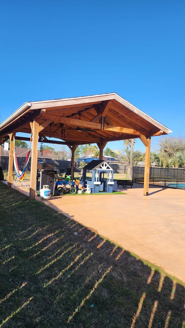 A covered outdoor area with a wooden structure, a hammock, a playhouse, and a pool. - Rexford Sound HideAway-Pool and Pet Friendly (Navarre)