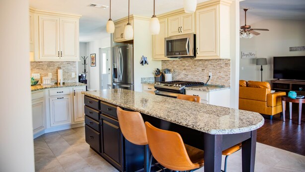 A modern kitchen with white cabinets, granite countertops, and a central island with bar stools. - Rexford Sound HideAway-Pool and Pet Friendly (Navarre)