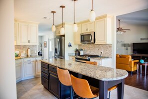 A modern kitchen with white cabinets, granite countertops, and a central island with bar stools. - Rexford Sound HideAway-Pool and Pet Friendly (Navarre)