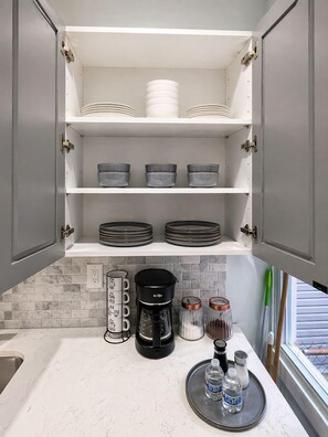 A kitchen with grey cabinets, a coffee maker, and a tray with water bottles. - Modern 2BR Apartment • Near Manhattan & PATH Train (Jersey City)