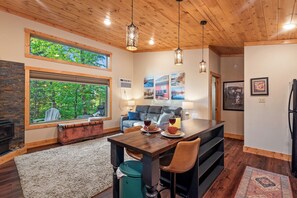 Ein gemütliches Wohnzimmer mit Kamin, eine Essecke mit Holztisch und Stühlen sowie ein großes Fenster mit Blick auf Grünflächen.