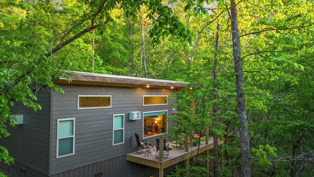 Uma cabana moderna com varanda, rodeada por uma floresta densa.