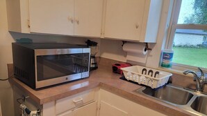 Cozinha com armários brancos, micro-ondas, cafeteira e pia.