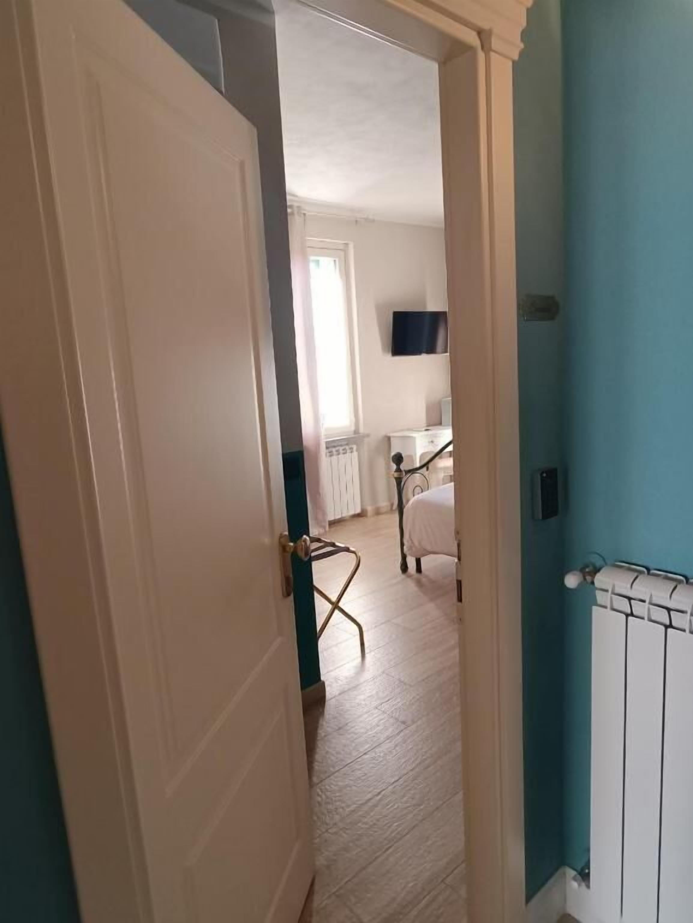 Un couloir étroit mène à une chambre où se trouvent un lit, un radiateur et un téléviseur fixé au mur.