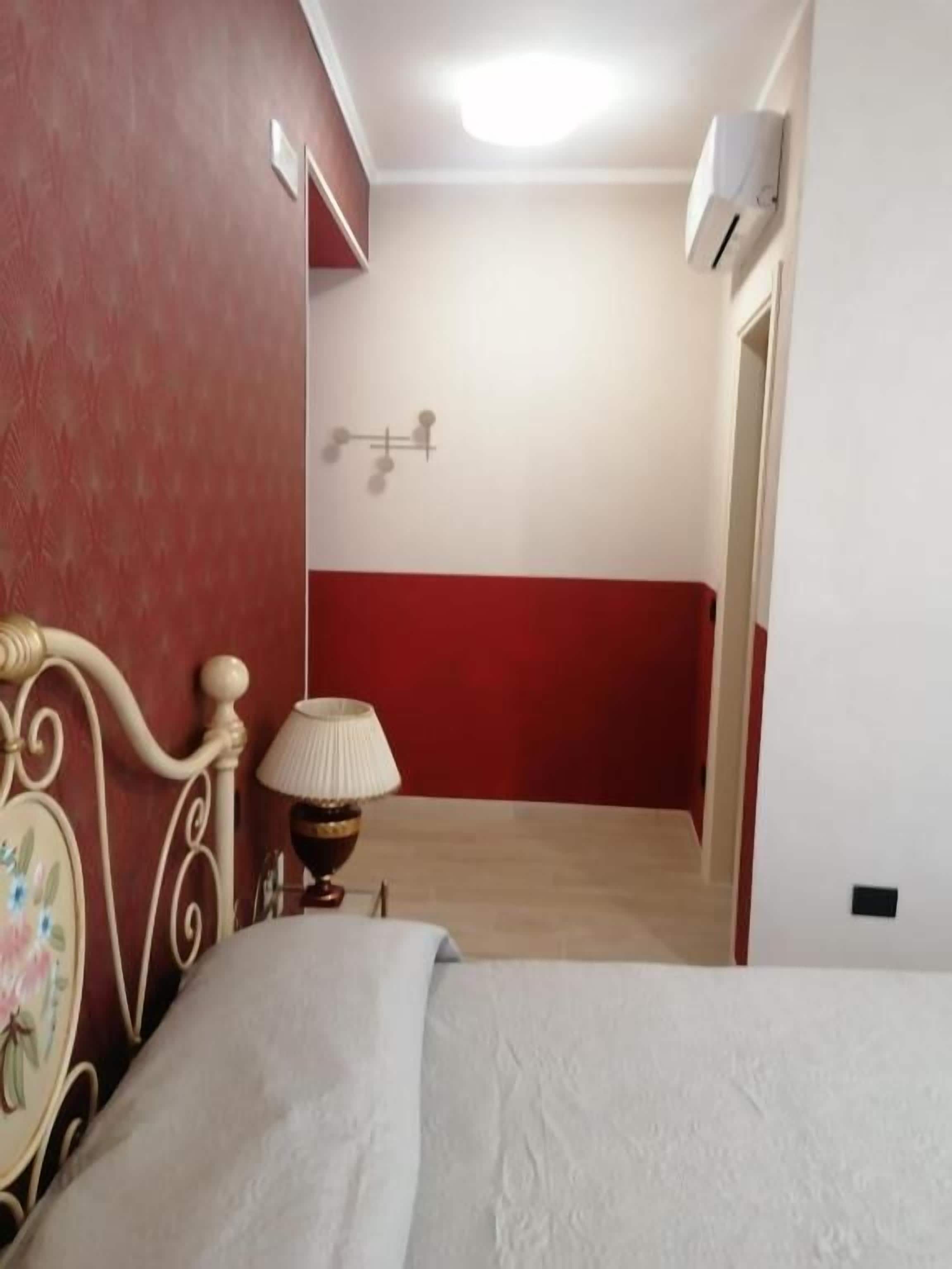 Une chambre d’hôtel avec un lit, une lampe, un climatiseur fixé au mur, et une décoration aux couleurs rouge et blanche.