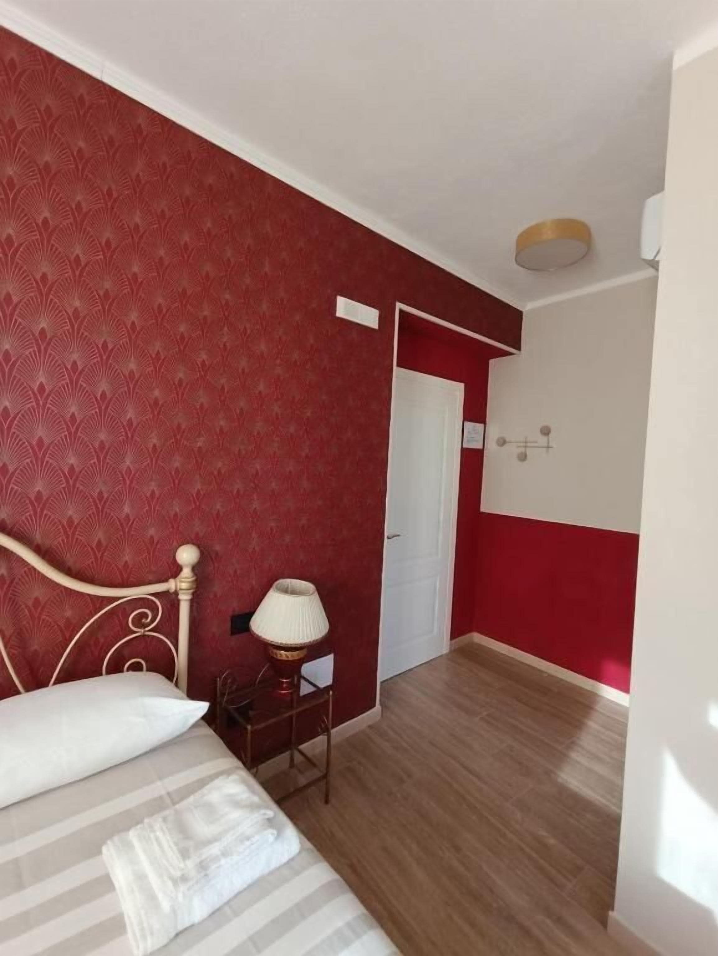 A room with a bed, a nightstand, a lamp, a door, and a red and white wall pattern.
