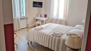 Een slaapkamer met een bed, bureau, stoel, televisie en een raam.