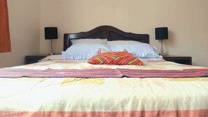 A bed with a colorful quilt, two bedside tables with lamps, and a wall-mounted picture. - Sumaq Wasi Inca Trails (Lima)