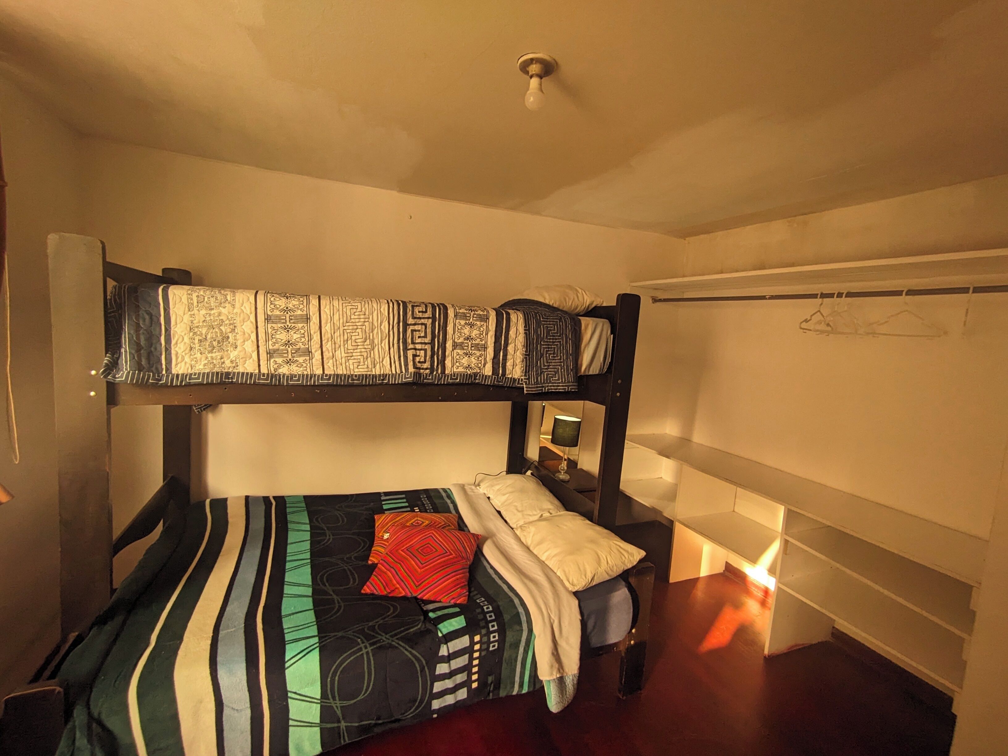 A bunk bed with patterned bedding, a bedside table with a lamp, and a wall-mounted shelf.