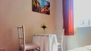 A hotel room with a bed, a small table with a vase of flowers, two white chairs, and a painting on the wall. - Sumaq Wasi Inca Trails (Lima)