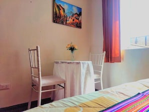 A hotel room with a bed, a small table with a vase of flowers, two white chairs, and a painting on the wall.