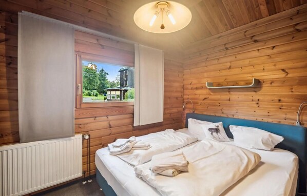A wooden-paneled room with a bed, a window with a view, and a ceiling light fixture. - Blockhaus im Harz fur Familien (Oberharz am Brocken)