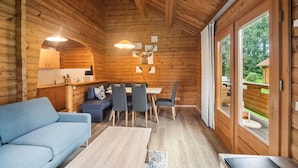 A wooden cabin interior with a sofa, dining table, chairs, and a kitchen area. - Blockhaus im Harz fur Familien (Oberharz am Brocken)