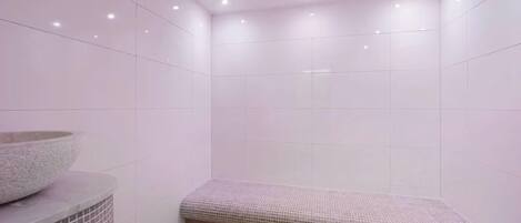 Un baño con paredes de azulejos blancos, un lavabo de piedra y un banco.