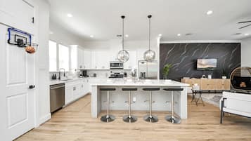 A modern kitchen with white cabinetry, a central island with bar stools, stainless steel appliances, and pendant lighting.
