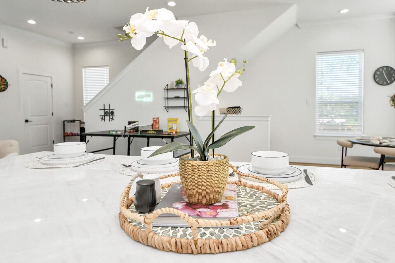 A modern dining area with a round table, white chairs, a woven centerpiece, and a view of the city through large windows.