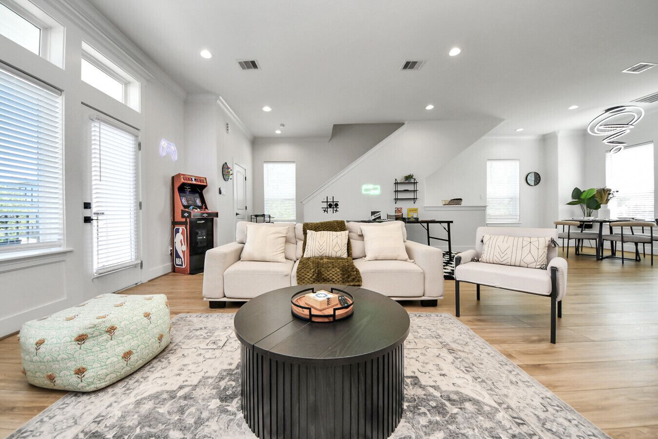 A spacious living area with a sofa, armchair, and coffee table, a dining area with a table and chairs, and a staircase leading to an upper level.