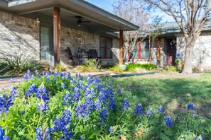 A house with a stone facade, a covered porch, and a lawn with blue flowers. - Waffle House | Pool · Game Room · Putting Green · (Abilene)