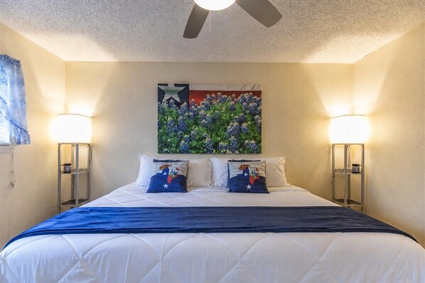 A hotel room with a bed, two bedside lamps, a ceiling fan, and a wall-mounted artwork. - Waffle House | Pool · Game Room · Putting Green · (Abilene)