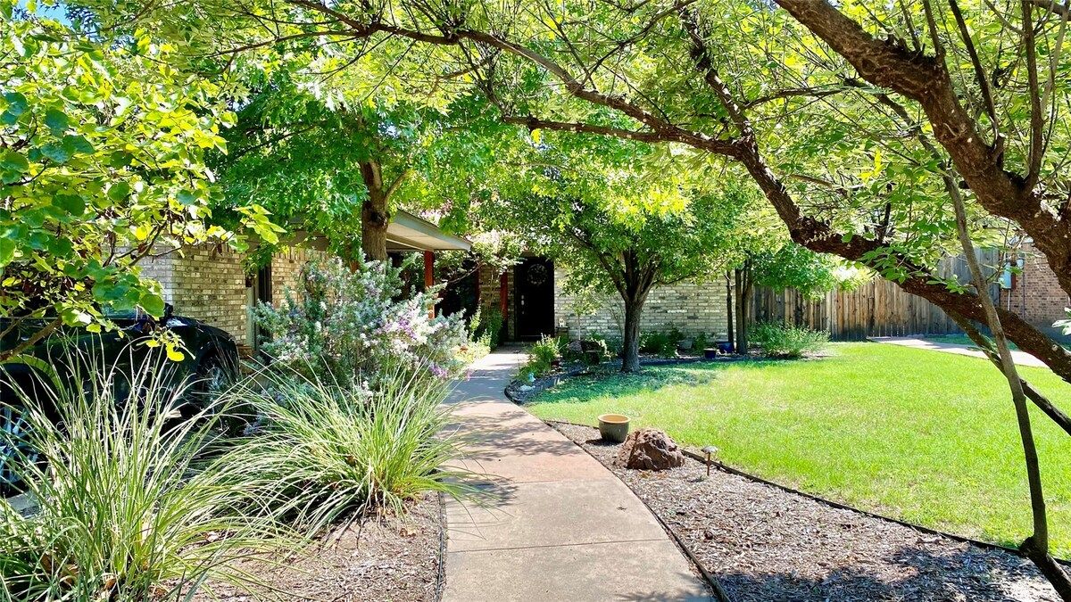 A residential backyard with a paved walkway, a lawn, and a brick house.