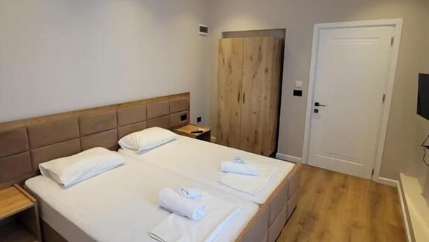 A bedroom with a large bed, wooden headboard, bedside tables, a wardrobe, and a door. - Te bunkeri (Ersekë)