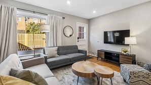 Ein modernes Wohnzimmer mit einem grauen Sofa, einem runden Couchtisch, einem Fernseher und einem Fenster mit Vorhängen.
