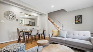Ein modernes Wohnzimmer mit einem grauen Sofa, einem Esstisch mit Stühlen, einem runden Couchtisch und einer Treppe.
