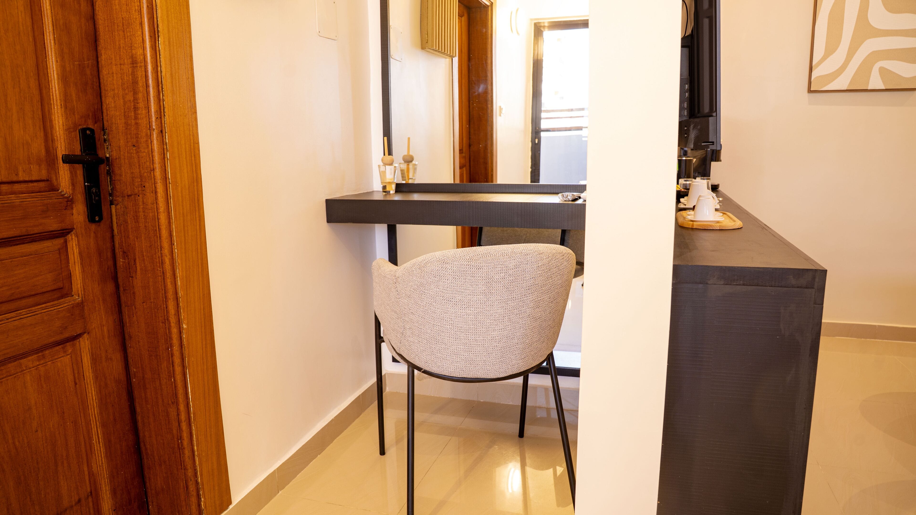 A hallway with a wooden door, a chair, a dark counter, and a coffee machine.
