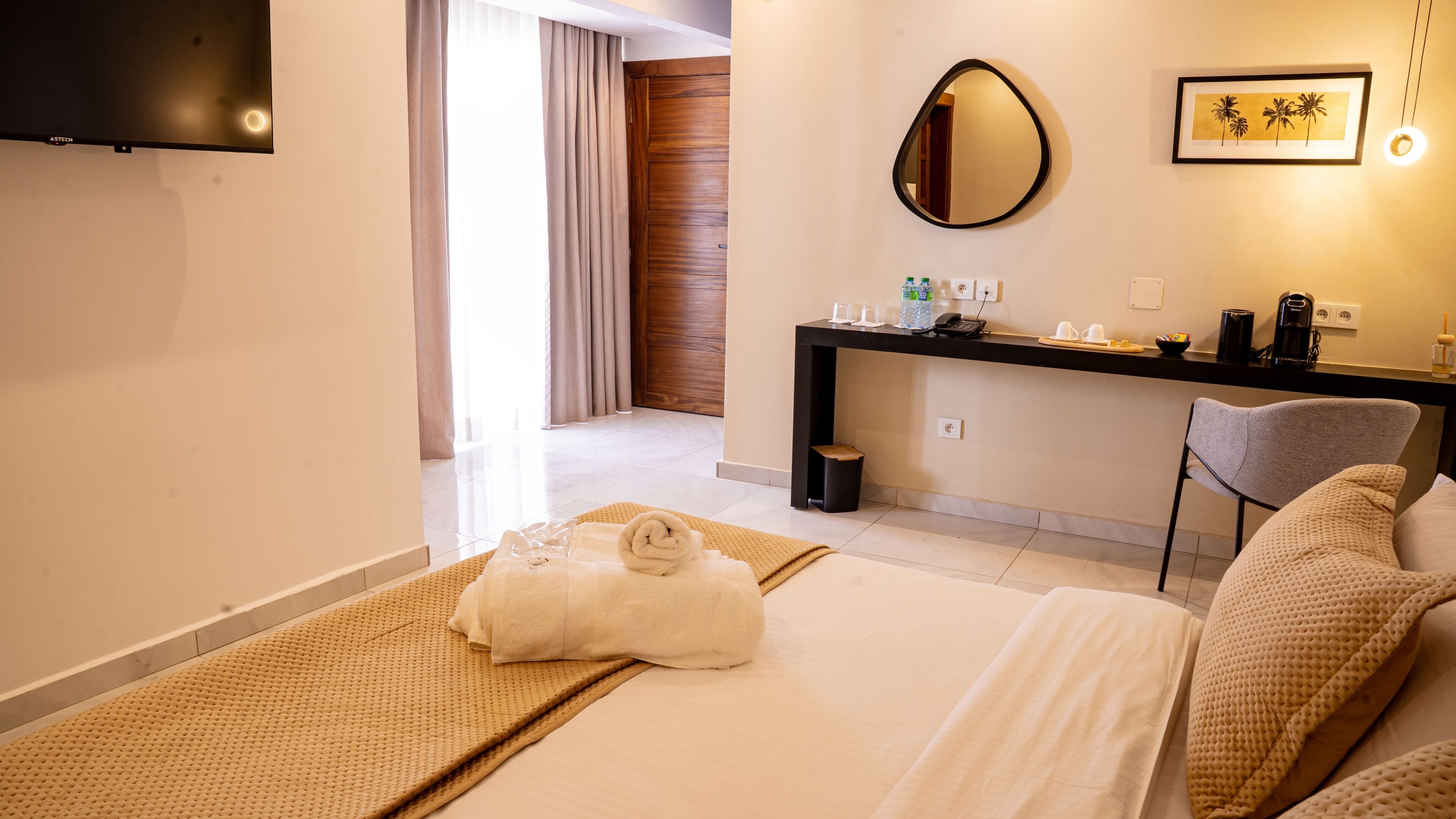 A hotel room with a bed, a desk, a chair, a mirror, and a TV.